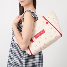 Model carrying Kate Spade Dash Floral Canvas Tote Bag in Cream Multi with red trim, floral print, and top zip fastening, styled with gingham dress