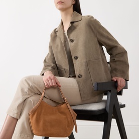 Model carrying Kate Spade Deco Tulip Small Suede Tote Bag in Garden Soil, tulip silhouette with top handles, styled with khaki jacket and trousers.