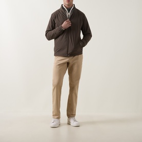 Model wearing Peter Millar Ryder 3-in-1 Jacket in Ash Brown with zip fastening, styled with beige chinos and white trainers.