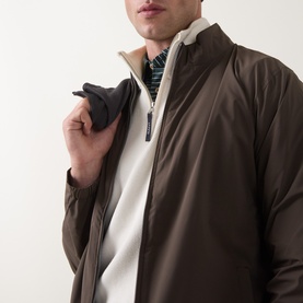Model wearing Peter Millar Ryder 3-in-1 Jacket in Ash Brown, styled with a white zip-neck knit and striped collar underneath