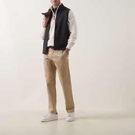 Model wearing Peter Millar Ryder 3-in-1 Jacket in Ash Brown, styled as gilet over white zip-neck layer, with tan chinos and white trainers.