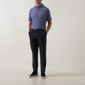 Model wearing Peter Millar Bali Blue polo shirt, styled with dark navy trousers, brown belt, and cream suede shoes.