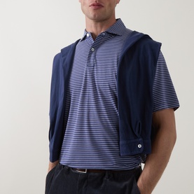Model wearing Peter Millar Bali Blue striped polo shirt, styled with a navy zip-up vest and dark trousers
