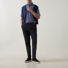 Model wearing Peter Millar Bali Blue polo shirt, styled with dark trousers, brown belt, and navy suede trainers.