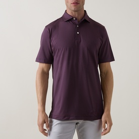 Model wearing Peter Millar polo in Bordeaux, short sleeves, three-button placket, styled with light grey trousers.