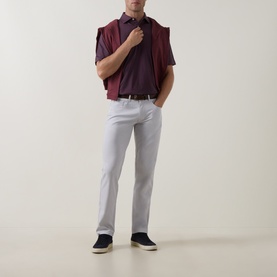 Model wearing Peter Millar polo in Bordeaux, styled with light grey trousers, dark navy loafers and a navy jacket draped over shoulder.