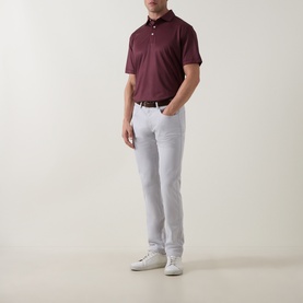 Model wearing Peter Millar bordeaux polo shirt, styled with white trousers and white trainers.