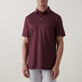 Model wearing Peter Millar polo shirt in Bordeaux, short sleeves and three-button placket, styled with light grey trousers.
