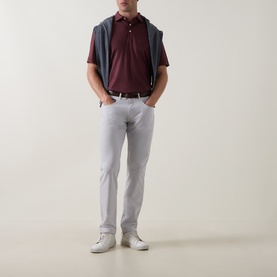 Model wearing Peter Millar Bordeaux polo shirt, styled with grey gilet, white slim-fit trousers and white trainers.