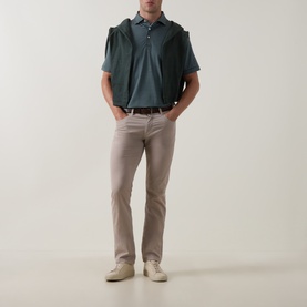 Model wearing Peter Millar polo in Pinebrook teal, styled with taupe trousers, brown belt, and cream trainers.