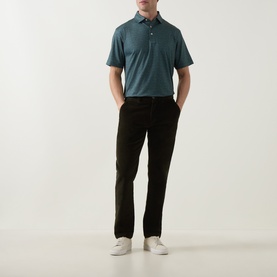 Model wearing Peter Millar polo in Pinebrook teal, styled with black trousers and white trainers