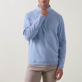 Model wearing Peter Millar Ardent Air Half-Zip Sweatshirt in Lakeside blue, with funnel neck and long sleeves, styled with beige trousers.