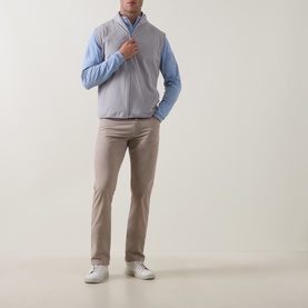 Model wearing Peter Millar Gale Grey quilted gilet over a light blue shirt, styled with taupe trousers and white trainers.