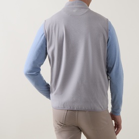 Model wearing Peter Millar Gale Grey sleeveless vest, back view, styled with light blue long-sleeve top and beige trousers.