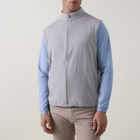 Model wearing Peter Millar Gale Grey zip-up vest over a blue long-sleeve top, with beige trousers.