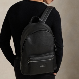 Model carrying Ralph Lauren black leather backpack with silver-tone hardware, front zip pocket, and logo plaque, worn over one shoulder