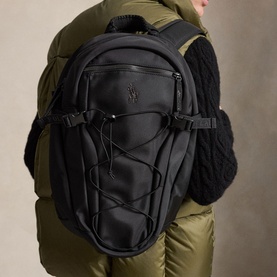 Model carrying Ralph Lauren black backpack with bungee cord front panel and embossed logo, styled with olive puffer jacket and knit scarf