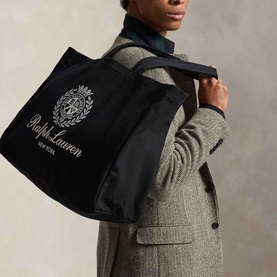 Model carrying Ralph Lauren Crest Logo Embroidered Canvas Tote Bag in black with white embroidered crest, styled with grey tweed coat