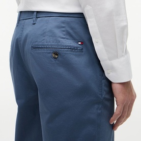 Model wearing Tommy Hilfiger Aegean Sea chino trousers, close-up of back pocket with logo flag detail, styled with a white shirt.
