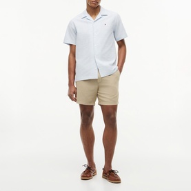 Model wearing Tommy Hilfiger Sandalwood shorts with a light blue short-sleeve shirt and brown lace-up boat shoes.