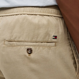 Model wearing Tommy Hilfiger sandalwood chino shorts, close-up of back pocket and elasticated waistband with flag logo badge.