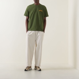 Model wearing Dickies Cypress green crew neck T-shirt with small chest graphic, styled with cream wide-leg trousers and beige trainers.