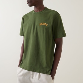 Model wearing Dickies Crew Neck T in Cypress green with arched logo print on chest, styled with white trousers.