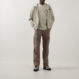 Model wearing Dickies Millville Logo T-Shirt in Eucalyptus, styled with a zip-up hoodie, brown cargo trousers and chunky trainers.