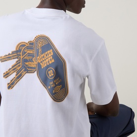 Model wearing Dickies white crew neck T-shirt, back view showing gold and navy motel key graphic print.