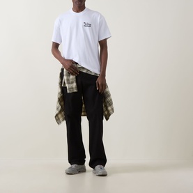 Model wearing Dickies white crew neck T-shirt with black trousers and plaid shirt tied at waist, grey trainers.