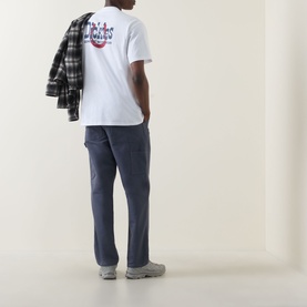Model wearing Dickies white crew neck T-shirt, back view with graphic print, styled with navy cargo trousers and grey trainers, plaid shirt draped