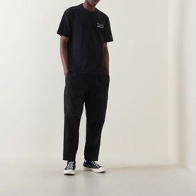Model wearing Dickies black cotton crew neck T-shirt with black cargo trousers and black and white canvas trainers.