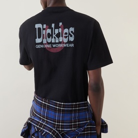 Model wearing Dickies black crew neck T-shirt, back view showing Genuine Workwear graphic print, styled with blue plaid shorts.