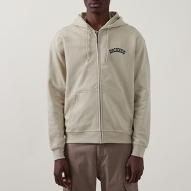 Model wearing Dickies Bettsville Logo Zip Hoodie in Eucalyptus with drawstring hood and front logo, styled with taupe trousers.