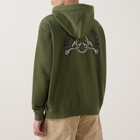 Model wearing Dickies Bettsville Logo Zip Hoodie in Cypress green, back view showing horseshoe graphic print, styled with beige trousers.