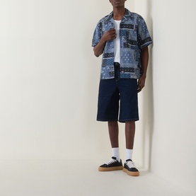 Model wearing Dickies rinsed navy cotton shorts, styled with blue patchwork print short-sleeve shirt, white tee, and black trainers.