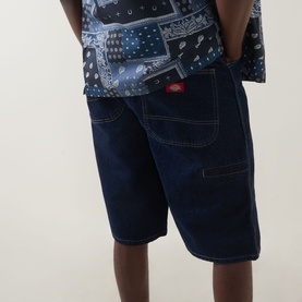 Model wearing Dickies rinsed denim shorts with contrast white stitching, styled with a blue bandana-print short-sleeve shirt.