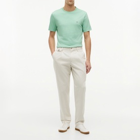 Model wearing Tommy Hilfiger Cut Grass green crew neck T-shirt with small chest logo, styled with cream chinos and white trainers.