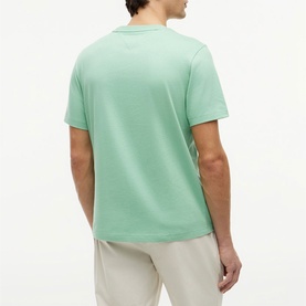 Model wearing Tommy Hilfiger Cut Grass green crew neck T-shirt, rear view, styled with light beige trousers.