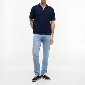 Model wearing Tommy Hilfiger Carbon Navy knit short-sleeve polo shirt, styled with light wash jeans and navy trainers.