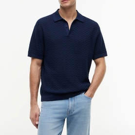 Model wearing Tommy Hilfiger Carbon Navy textured knit polo shirt with open collar, styled with light blue jeans.