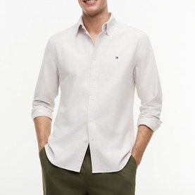 Model wearing Tommy Hilfiger Coastal Taupe stripe long-sleeve shirt with chest logo, styled with olive green trousers.