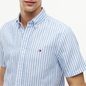 Model wearing Tommy Hilfiger short-sleeve shirt in Blue Spell stripe, button-down collar, with embroidered flag logo at chest.