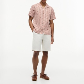 Model wearing Tommy Hilfiger short-sleeve printed shirt in Rusty Ochre with white shorts and brown boat shoes.