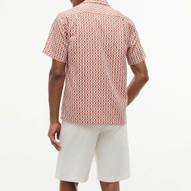 Model wearing Tommy Hilfiger shirt in Rusty Ochre geometric allover print, short sleeves, camp collar, styled with white shorts, back view.
