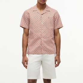 Model wearing Tommy Hilfiger short-sleeve shirt in Rusty Ochre allover print, camp collar, styled with white shorts.