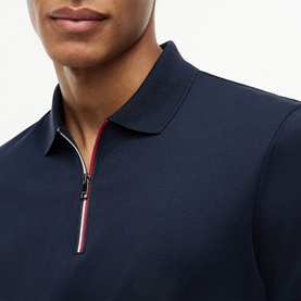 Model wearing Tommy Hilfiger navy blue polo shirt with quarter-zip collar detail featuring red and white stripe trim.