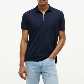 Model wearing Tommy Hilfiger navy blue zip-collar polo shirt, styled with light blue jeans.