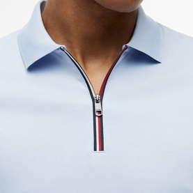 Model wearing Tommy Hilfiger Breezy Blue polo shirt, close-up of zip placket with signature red, white and navy stripe detail.