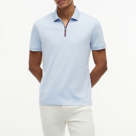 Model wearing Tommy Hilfiger Breezy Blue quarter-zip polo shirt with striped zip detail, styled with white trousers.